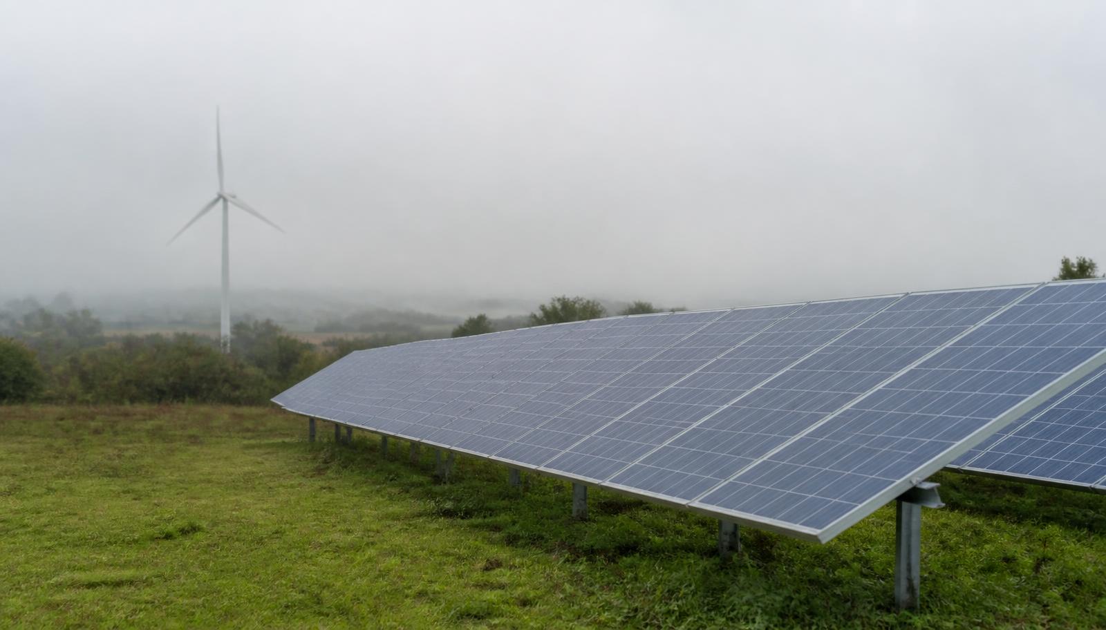 Ground-mounted solar array with a wind turbine in the distance